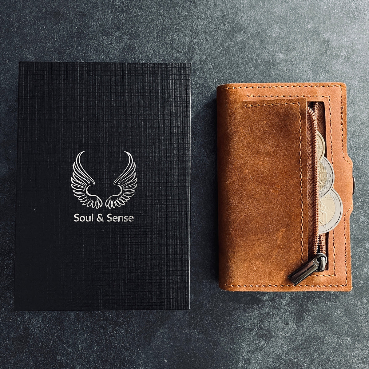 Soul & Sense Wallet aus Leder neben der Marken-Box auf dunklem Schiefer